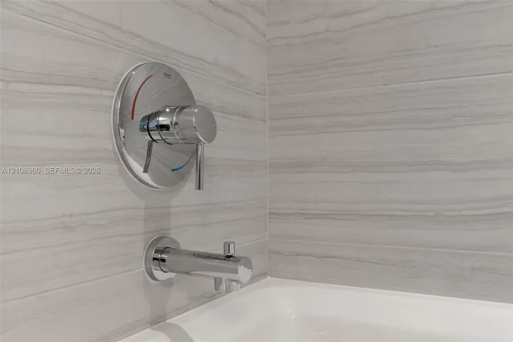Linear-patterned stone tile surround, polished chrome single-handle faucet, integrated tub spout, and white porcelain bathtub