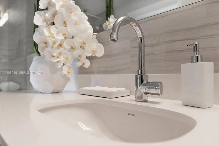 Undermount oval sink with a polished chrome faucet and solid-surface countertop, complemented by horizontal-veined stone wall tile and a full-width mirror