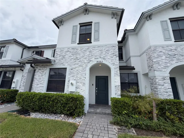 Multi-story exterior featuring a textured stone veneer facade, a recessed entryway with a stone-paved walkway, and dark-framed windows with decorative shutters
