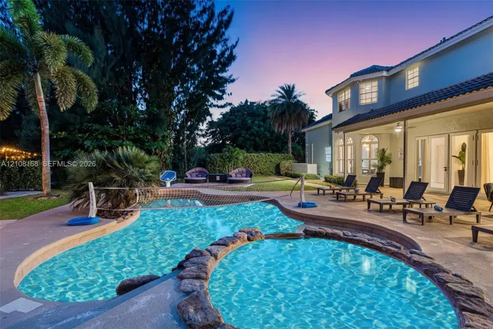 Freeform swimming pool with a rock-bordered spa, covered patio, concrete deck, and mature landscaping
