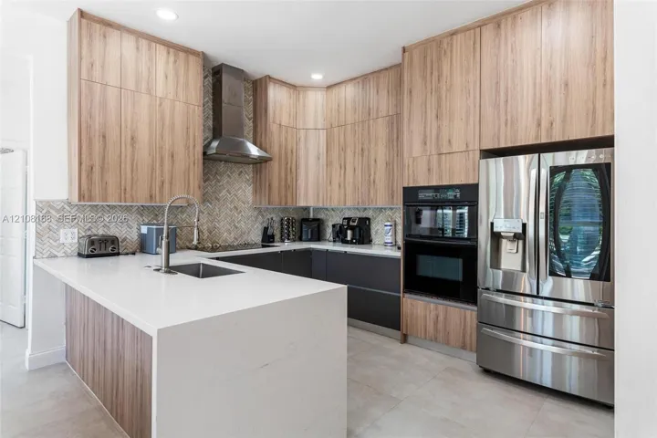 Kitchen featuring wood-finish cabinetry, stone-surface countertops, a herringbone tile backsplash, stainless steel appliances, and a built-in oven