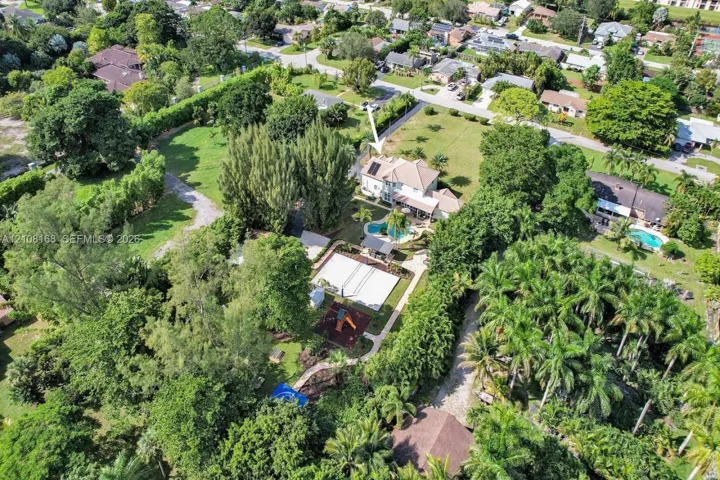 Aerial perspective of a multi-story residence featuring an in-ground swimming pool, a hardscaped sport court, extensive mature landscaping, and solar roof panels