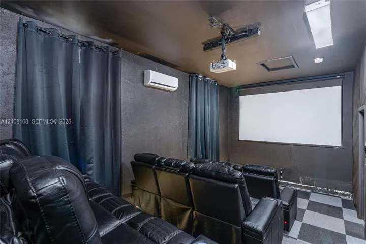 Media room featuring a mounted projection screen, ceiling-mounted digital projector, wall-mounted ductless air conditioning unit, and checkered tile flooring