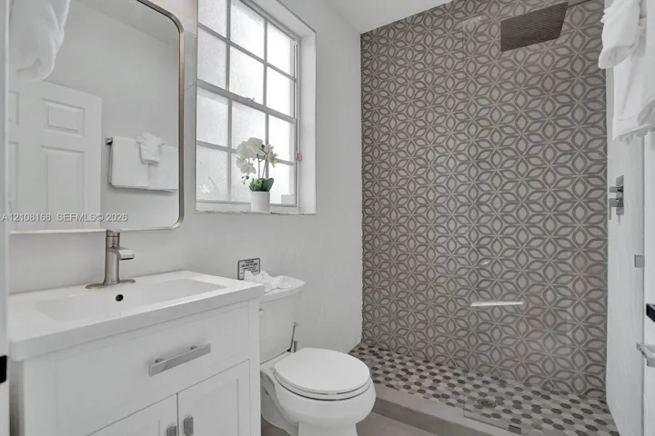 Bathroom featuring a white vanity cabinet with a rectangular basin, patterned geometric tilework in the walk-in shower, recessed ceiling-mounted shower head, glass shower panel, and a grid-pane window