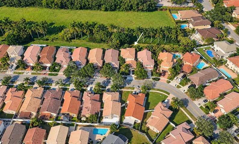 Aerial perspective of a residential property featuring a tiled roof, multi-car garage, perimeter fencing, and mature palm trees