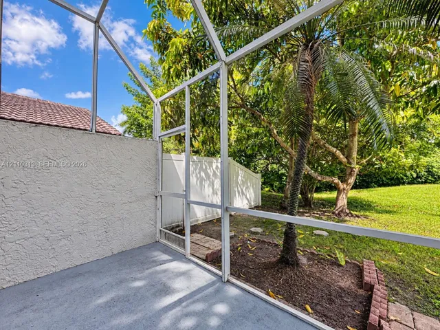 Screened-in patio featuring a concrete floor, stucco wall, white aluminum framing, and direct access to a grassy yard with mature palms and vinyl privacy fencing