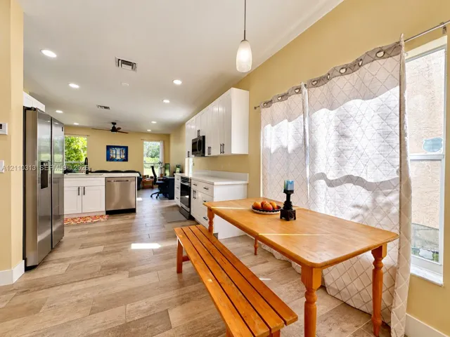 Kitchen featuring white shaker-style cabinetry, stainless steel appliances, wood-finish tile flooring, recessed lighting, and a pendant light fixture
