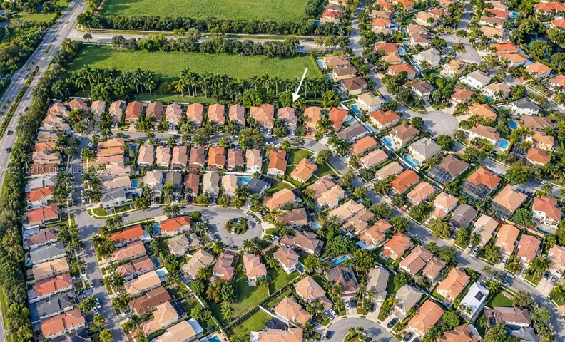 Aerial perspective of a residential community featuring tile-roofed architecture, paved street grids, landscaped green spaces, and dense perimeter foliage