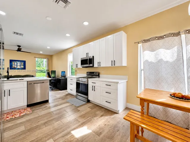Kitchen featuring white Shaker-style cabinetry, stainless steel appliances, solid-surface countertops, and wood-finish flooring