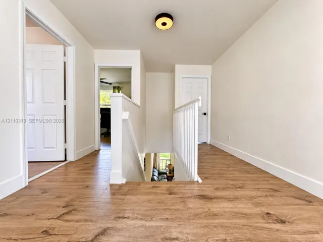 Landing area featuring wood-finish flooring, white paneled interior doors, a white wooden staircase railing, and a circular flush-mount ceiling light fixture
