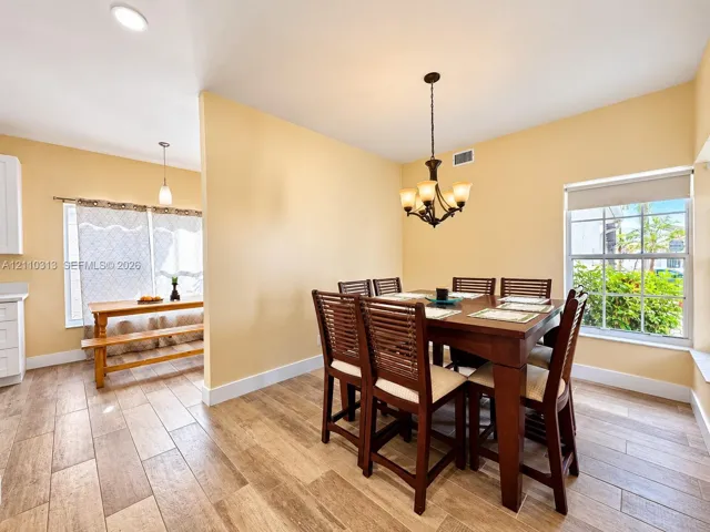 Wood-finish tile flooring, multi-light chandelier, recessed lighting, and large windows providing natural illumination
