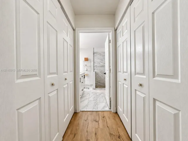 Hallway featuring four white multi-panel bi-fold doors, wood-finish flooring, and stone-tile flooring in the interior space