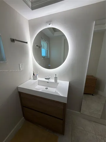 Modern vanity with a rectangular integrated sink, wood-finish cabinetry, circular LED backlit wall mirror, and floor-to-ceiling wall mirror