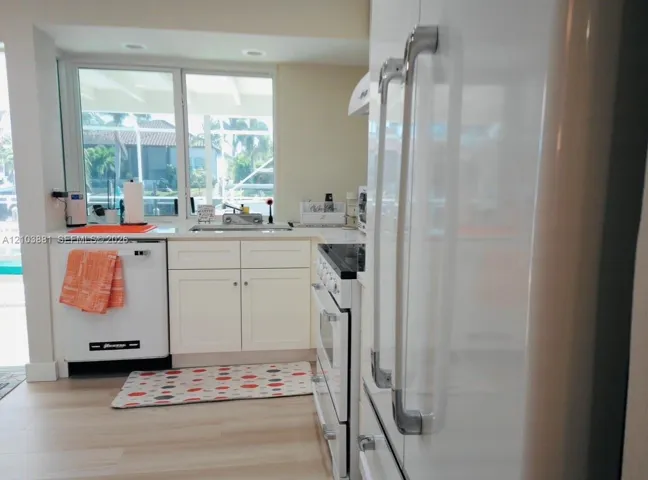 Kitchen featuring white cabinetry, solid-surface countertops, wood-finish flooring, and white appliance suite including a range and dishwasher