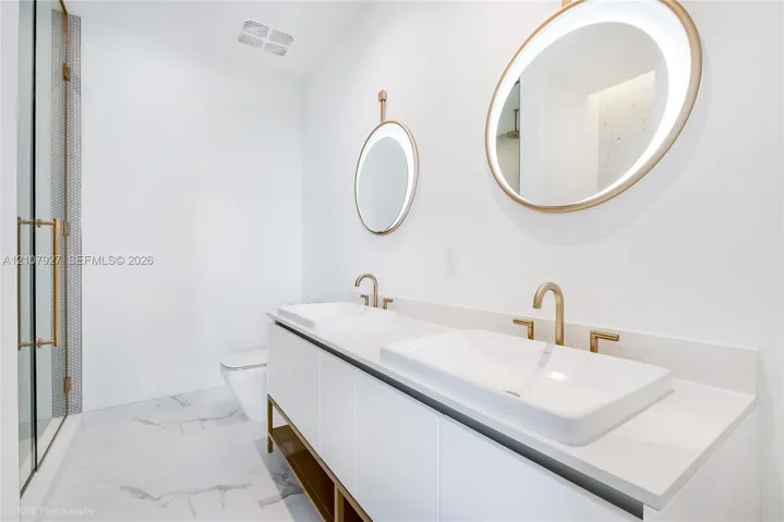 Dual-sink vanity featuring stone-composite countertops, integrated vessel sinks, and brass-tone hardware