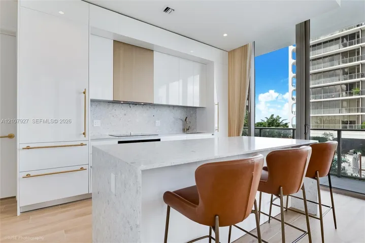 Modern kitchen featuring high-gloss cabinetry, a stone-surfaced waterfall island, integrated appliances, and wood-finish flooring