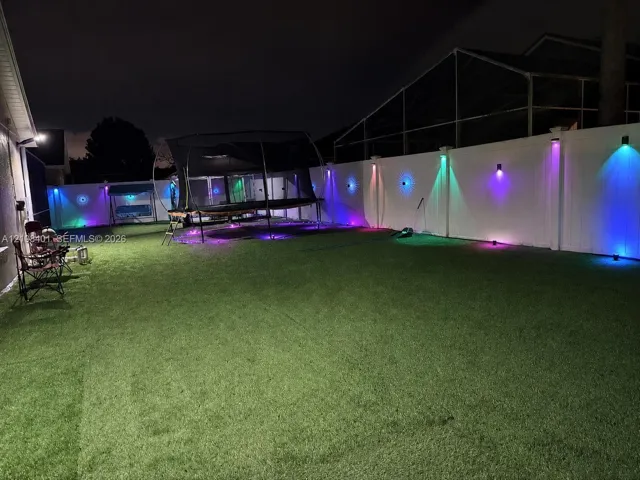 Fenced backyard featuring synthetic turf, privacy screening, and wall-mounted exterior accent lighting