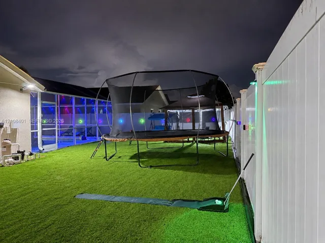 Backyard featuring synthetic turf, white vinyl privacy fencing, and an attached screened-in enclosure