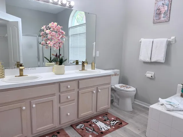 Double vanity featuring light wood cabinetry, quartz countertops, dual undermount sinks with brushed gold faucets, and an arched window