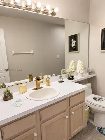 Bathroom vanity featuring a light-tone wood cabinet, integrated countertop with an oval basin, brass-finish faucet, and a wall-mounted light fixture