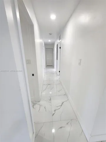 Hallway featuring large-format tile flooring with veined detailing, recessed ceiling lighting, and crisp white wall finishes