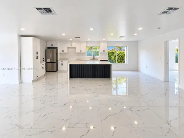 Open-concept kitchen featuring polished stone-finish flooring, white cabinetry, a center island with a black ribbed base, recessed lighting, and stainless steel appliances