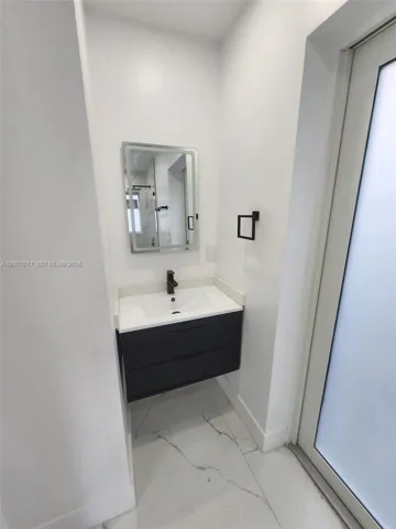 Wall-mounted vanity featuring dual drawers, integrated rectangular sink, stone-finish countertop, matte black faucet, and backlit rectangular mirror, complemented by large-format tile flooring
