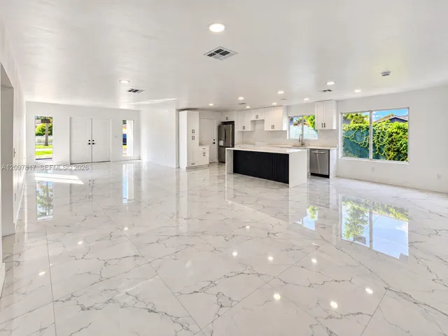 Open-concept interior featuring large-format tile flooring, recessed lighting, white cabinetry, and a kitchen island with a contrasting dark base and white countertop
