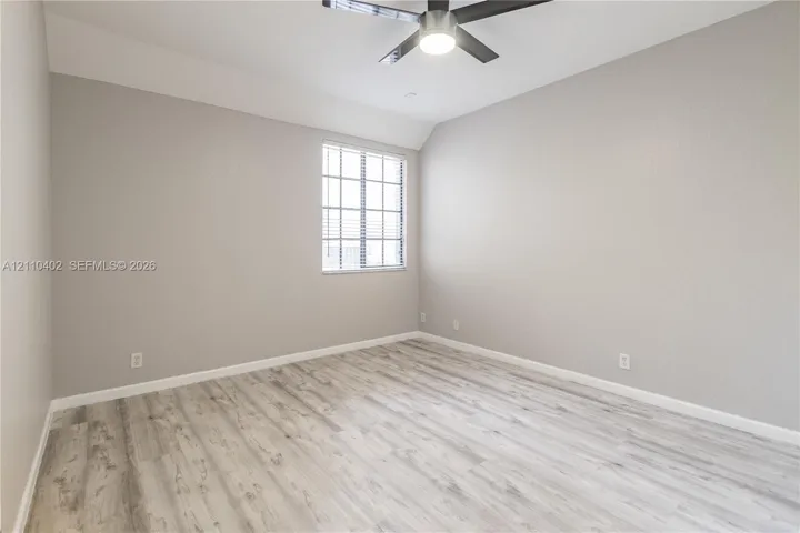 Room with wood-finish flooring, neutral wall paint, multi-pane window, and a ceiling fan with integrated lighting