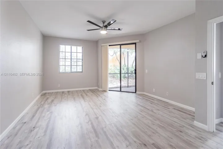 Neutral-toned interior featuring wood-finish flooring, a multi-pane window, a ceiling-mounted light fixture with fan, and a sliding glass door