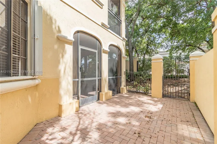 Stucco exterior featuring arched screened entryways, a herringbone-patterned brick patio, and a decorative metal gate enclosure