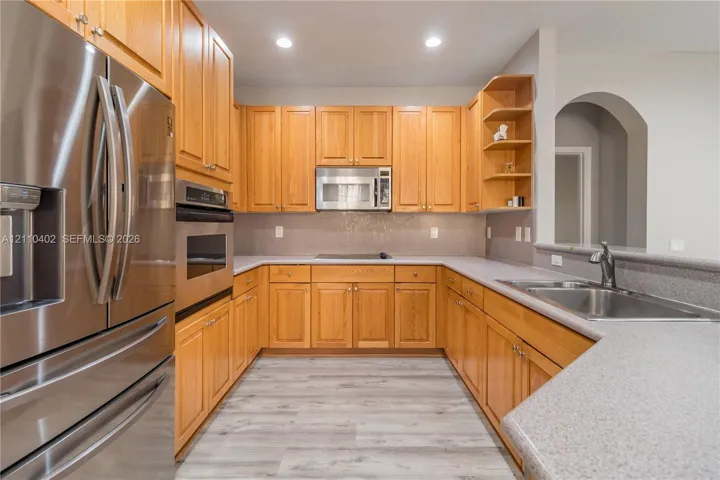 Kitchen featuring light wood cabinetry, stainless steel appliances, solid surface countertops, recessed lighting, and wood-finish flooring