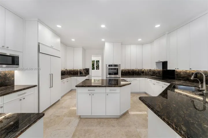 Kitchen featuring white cabinetry, stone countertops, a central island, built-in stainless steel appliances, and stone flooring