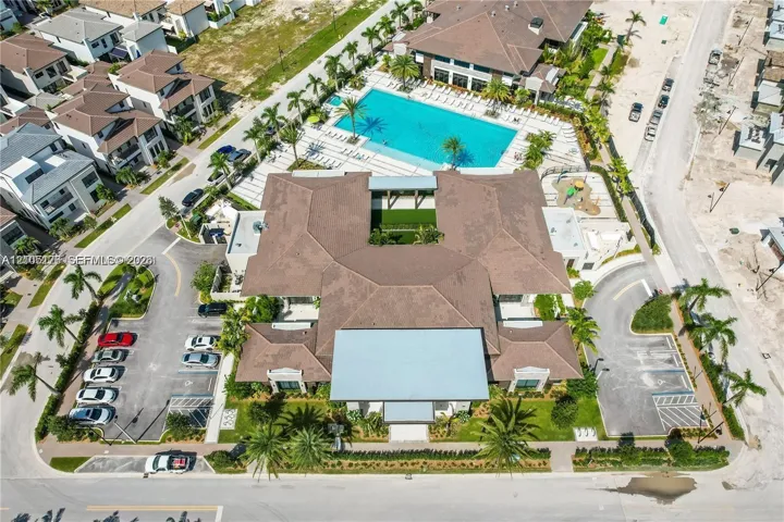 Community center featuring a multi-lane swimming pool, landscaped central courtyard, paved surface parking, and curated palm tree installations