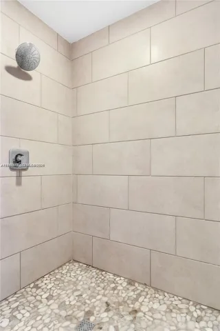 Shower featuring large-format ceramic wall tile, natural stone pebble flooring, and a rainfall showerhead