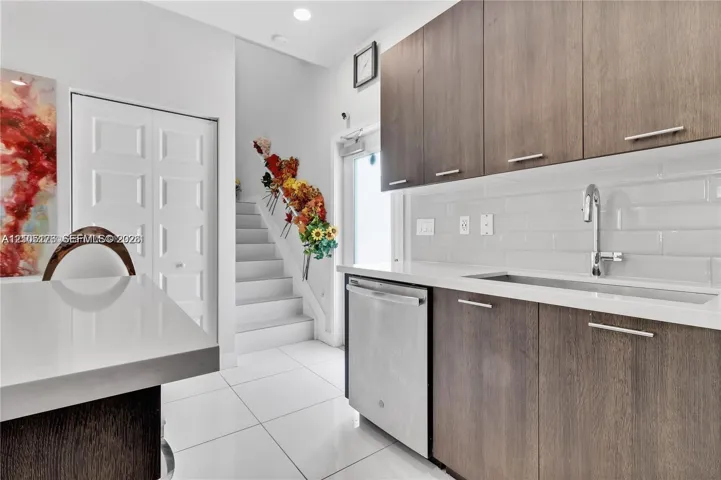 Flat-panel wood-finish cabinetry, white solid-surface countertops, stainless steel undermount sink with arched faucet, white subway tile backsplash, and polished tile flooring