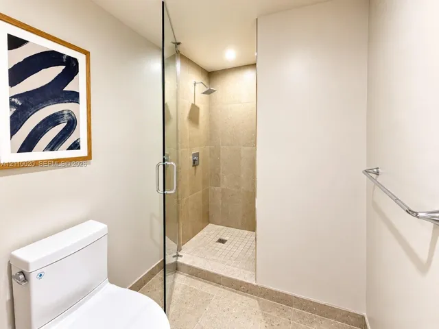 Walk-in shower featuring a frameless glass door, neutral-toned large-format tile surround, square rainfall showerhead, and a matching tiled floor