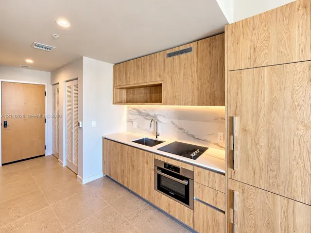 Kitchen area featuring wood-finish cabinetry, solid surface countertops, integrated appliances, stone-patterned backsplash, and recessed lighting