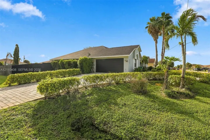 Single-story residence featuring a shingled roof, paver driveway, attached two-car garage, and established tropical landscaping