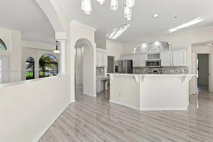 Kitchen featuring wood-finish tile flooring, white cabinetry, a breakfast bar with decorative corbels, stainless steel appliances, and arched architectural entryways