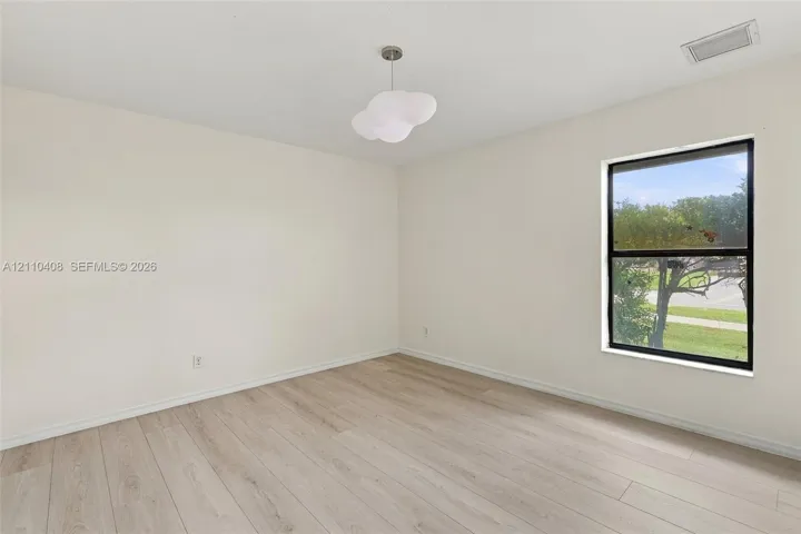 Neutral-toned interior featuring wood-finish flooring, a single-pane window, and a modern sculptural pendant light fixture