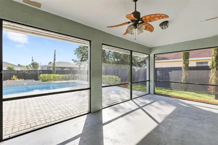 Screened-in patio featuring a vaulted ceiling with a palm-blade paddle fan, concrete flooring, large window panels, and direct exposure to a paved pool deck