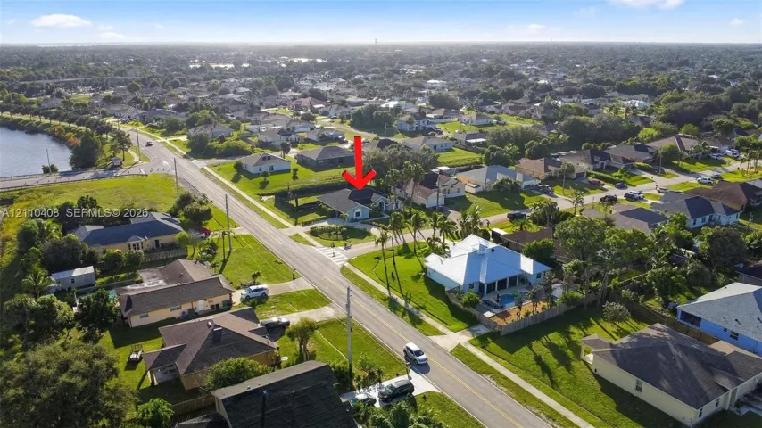Aerial perspective of residential property featuring a hip roofline, concrete driveway, and expansive lawn area within a suburban setting