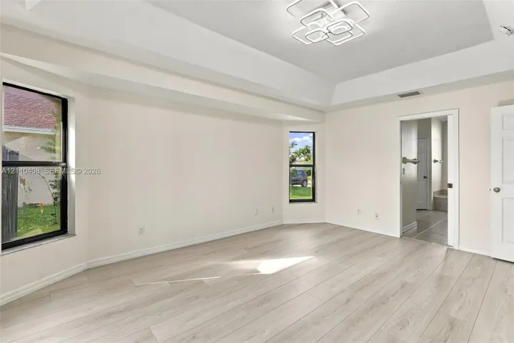 Room featuring a tray ceiling, wood-finish flooring, dual windows, and a multi-tiered geometric LED light fixture
