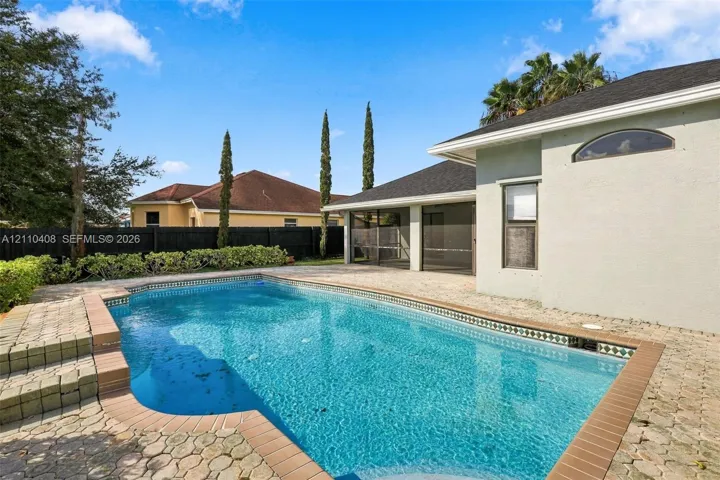 In-ground swimming pool with tile border and concrete paver decking, enclosed screened-in lanai, and fenced perimeter