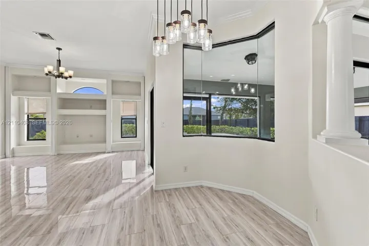 Open-concept interior featuring wood-finish flooring, a multi-light glass pendant fixture, built-in shelving, an angular window design, and a classic architectural column
