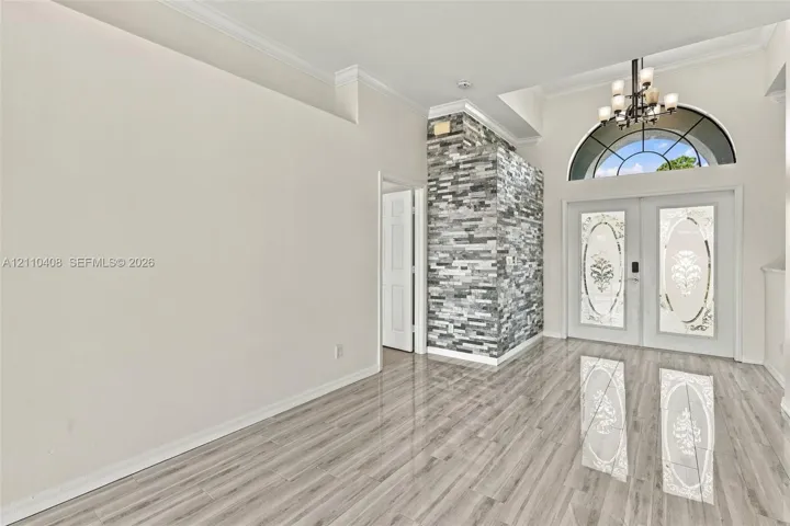 Entryway featuring high ceilings, wood-finish flooring, dual doors with decorative glass inserts, an arched transom window, and a floor-to-ceiling textured stone accent wall