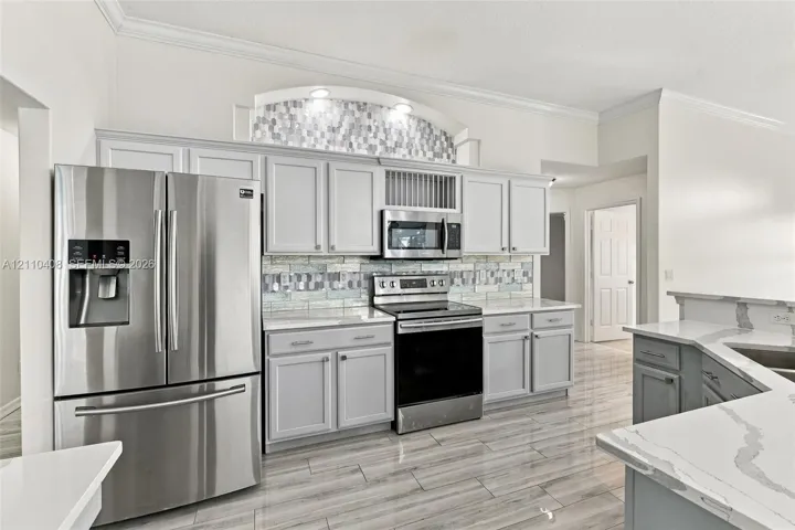 Kitchen featuring light gray cabinetry, stainless steel appliances, patterned tile backsplash, decorative arched alcove with integrated lighting, and white stone-finish countertops with veining