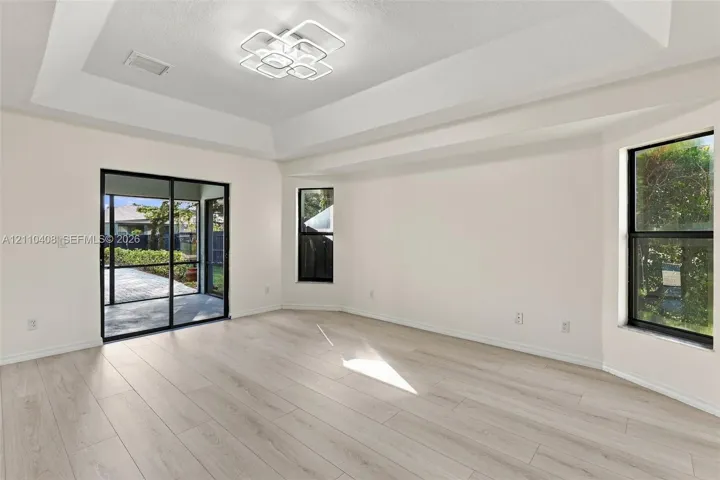 Tray ceiling featuring a geometric flush-mount light fixture, light wood-finish flooring, and sliding glass doors with black frames