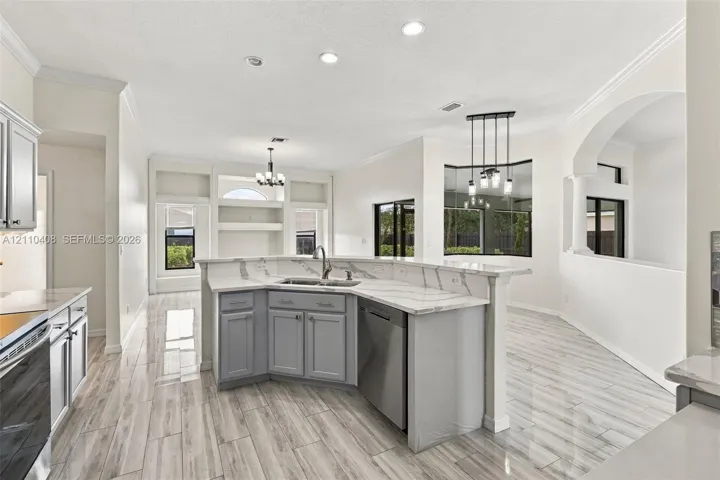 Kitchen featuring a peninsula with solid-surface countertops, grey cabinetry, stainless steel dishwasher, wood-finish flooring, and built-in shelving